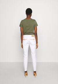 Olivgrön kortärmad topp med stjärnprydnader, i kombination med vita tajta byxor som har hög midja och distinkta fickdetaljer.