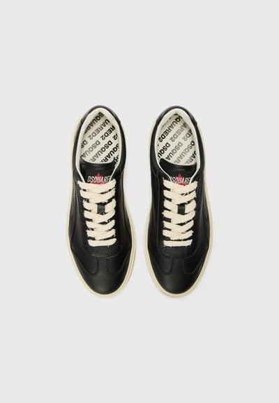 Zapatillas negras de cuero con un acabado suave, cordones beige y una suela de goma crema en contraste. El interior cuenta con una plantilla de marca.