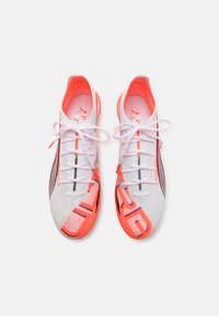 White athletic shoes with bright orange accents and black detailing. Features mesh material, flat laces, and a patterned sole.