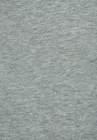 Primer plano de la textura de tela gris claro con patrón de punto fino y costuras visibles en el borde inferior.
