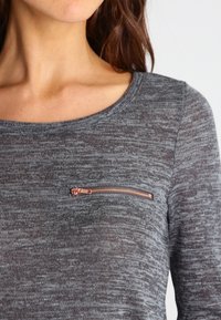 Maglia a maniche lunghe grigia con texture, scollatura rotonda e una piccola tasca sul petto con dettagli in cerniera color oro rosa.