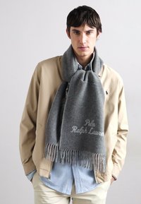 Szürke gyapjú sál felszegélyezett szélekkel, a "Polo Ralph Lauren" hímzett logójával, bézs zakóra és világoskék ingre felvéve.