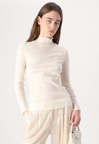 Top a maniche lunghe color crema con un tessuto trasparente e testurizzato e un collo a camicia arricciato. Abbinato a pantaloni beige chiaro con paillettes.