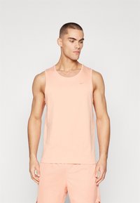 Lyserød tanktop lavet af blødt stof, med en rund halsudskæring og et diskret Nike-logo i bronze på brystet.