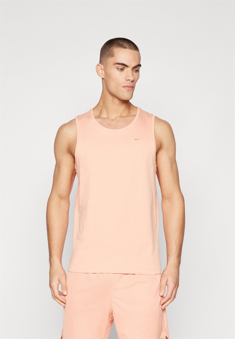 Lyserød tanktop lavet af blødt stof, med en rund halsudskæring og et diskret Nike-logo i bronze på brystet.