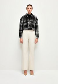 Chaqueta de cuadros en blanco y negro, recortada y con cuello, combinada con pantalones de pierna ancha color crema y tacones de punta beige. Texturas suaves en general.