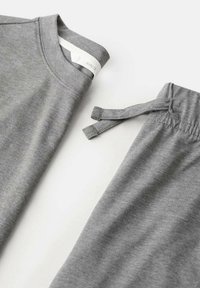 Camiseta gris de algodón con cuello redondo y pantalones deportivos grises a juego que cuentan con una cinturilla elástica y cordones.