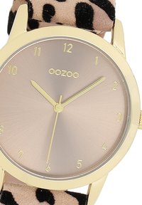 Montre-bracelet dorée avec un cadran métallique rose doré, bracelet en cuir noir à motif léopard et marqueurs d'heure minimalistes.