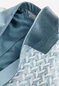 Colletto di giacca blu con tessuto a motivo geometrico, dettaglio in suede blu scuro e rivestimento interno liscio a righe blu.