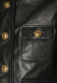 Černá kožená bunda s velkou náprsní kapsou a zlatými knoflíky s designem lana. Hladká textura s lesklým povrchem.