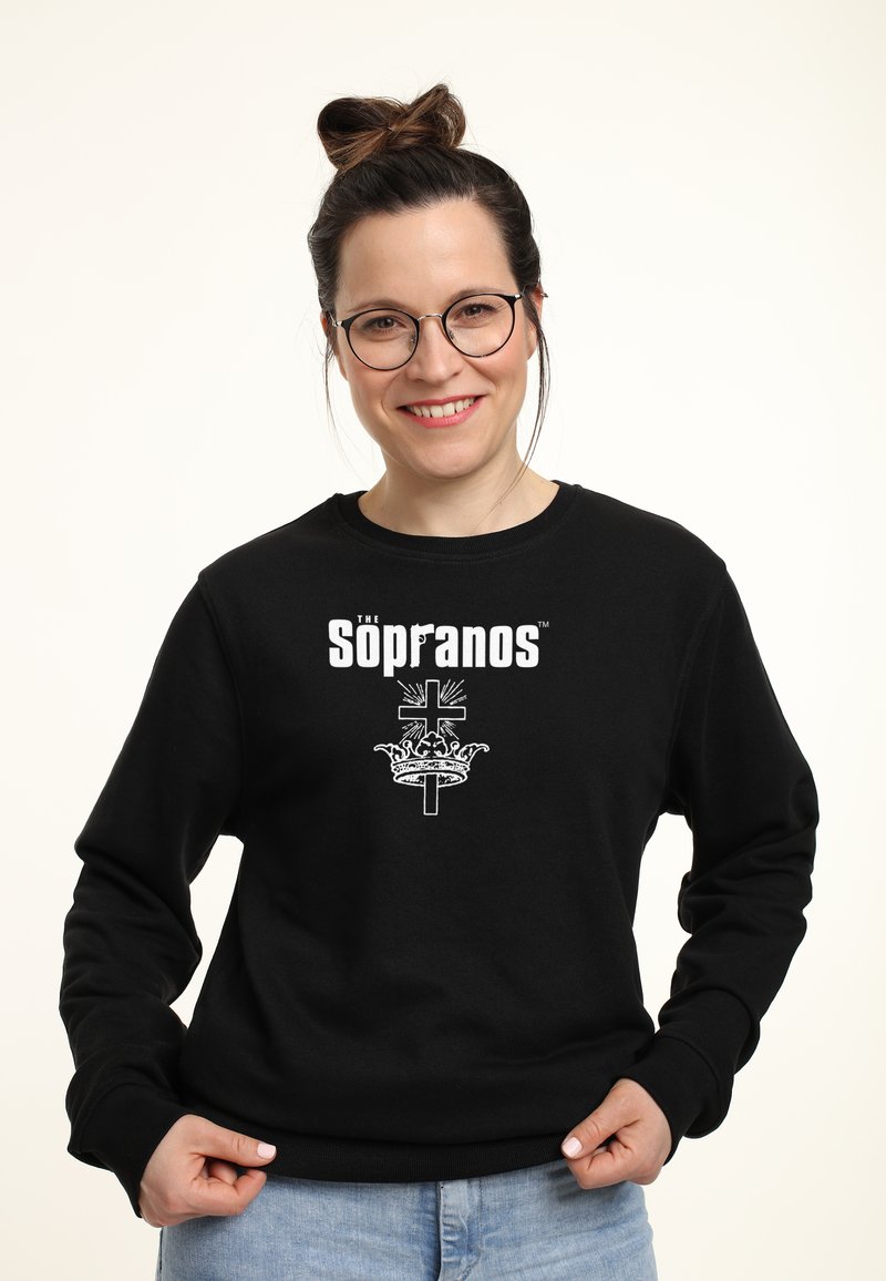 Felpa nera con il testo "The Sopranos" in bianco sopra un grafico di una corona e una croce. Il tessuto appare texturizzato e morbido.