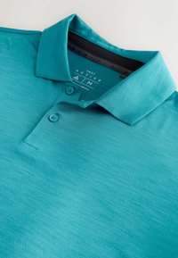 Polo à manches courtes bleu sarcelle avec deux boutons et un col plié, étiqueté "Next Active" en taille moyenne.