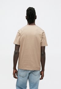 T-shirt met korte mouwen en ronde hals in licht beige katoen. Gladde textuur, comfortabele pasvorm, eenvoudig ontwerp zonder zichtbare patronen of accenten.