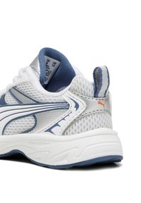 Baskets blanches et bleues avec une tige en maille, un col rembourré, une semelle texturée et un petit logo orange sur le talon.