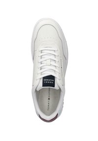 Witte sneaker met glad leer, ronde neus, geperforeerde textuur, toon-op-toon stiksels, platte veters en een marineblauw label met de merknaam.