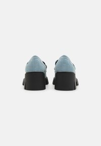 Light blue canvas shoes with a black thick sole, featuring a rounded toe and minimal stitching details. Back view shows a structured design.
