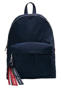 Sac à dos en nylon bleu marine avec un dessus arrondi, une fermeture éclair argentée, une poche avant, et une étiquette de marque rouge et blanche. Dispose de bretelles réglables.
