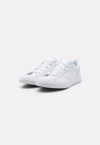 Zapatillas blancas hechas de material sintético suave, con puntera redondeada, cordones planos y un sutil logo de estrella en el costado.