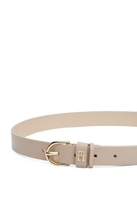 Beige nahkavööd koos kullatooni metallist pandlaga, millel on logomuster ja mitu reguleerimisauku rihma ääres. Lame ja sile tekstuur.