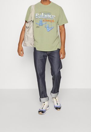 T-shirt en coton vert avec imprimé graphique, jean en denim foncé, baskets de couleur claire et un sac fourre-tout en toile beige. Tenue décontractée.