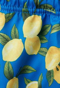 Swimwear fabric featuring large yellow lemons with green leaves on a bright blue background. Smooth texture with elastic stitching detail.