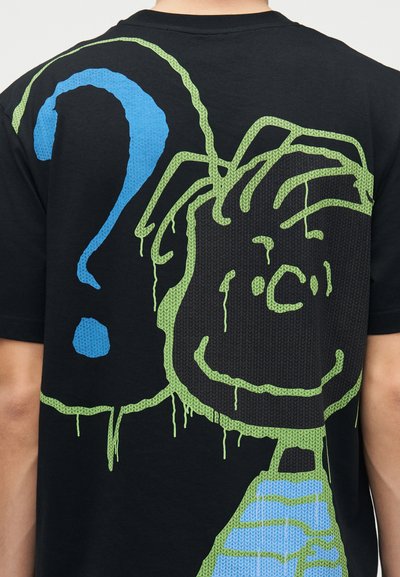 T-shirt noir avec un personnage de dessin animé vert et bleu dégoulinant et un grand point d'interrogation bleu dans le dos.