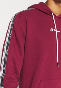 Felpa Burgundy Champion con coulisse bianche, tasca frontale e strisce nere e bianche con marchio sulla manica.