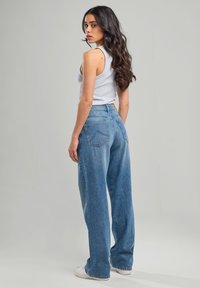 Top sin mangas de color gris claro combinado con jeans de denim azul de tiro alto y corte holgado. Los jeans tienen un aspecto desgastado y bolsillos traseros con detalle de costura.