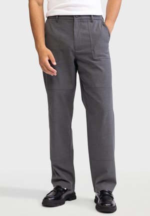 Pantalones grises ajustados con un acabado de tela suave, que cuentan con dos bolsillos frontales y un diseño de pierna recta. Combinados con zapatos negros.