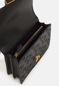 Zwarte leren handtas met reliëfpatroon, gouden ritsdetails en een ronde gouden sluiting. Interieur bevat een ritsvak.