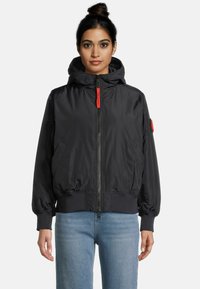 Veste bomber noire à capuche avec fermeture éclair frontale, poignets et taille élastiques. Tirette de fermeture éclair rouge remarquable et poches latérales. Matériau lisse et brillant.