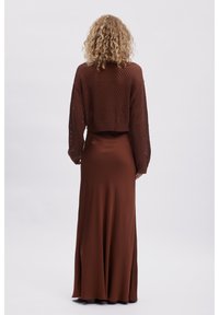 Bruine gebreide cropped sweater met een open weefpatroon en lange mouwen, gecombineerd met een elegante, vloerlange bruin satijnen rok.