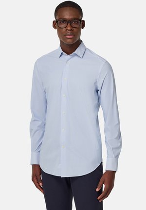 Camisa de vestir a rayas azul claro con mangas largas, collar abotonado y dobladillo curvado. La tela parece suave y ligera.