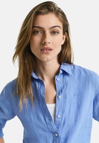 Lichtblauwe, knoopsluiting linnen shirt met opgerolde mouwen en subtiele stiksels. Heeft een klassieke kraag en knopen aan de voorkant.