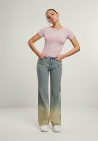 Lyserød tettsittende t-skjorte med korte ermer og hvit logo, sammen med lyseblå jeans med gradiert falming til lys beige ved mansjettene.