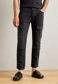 Pantaloni cargo neri in denim con molteplici tasche applicate, design a gamba dritta e leggere usure. Abbinati a zoccoli neri.