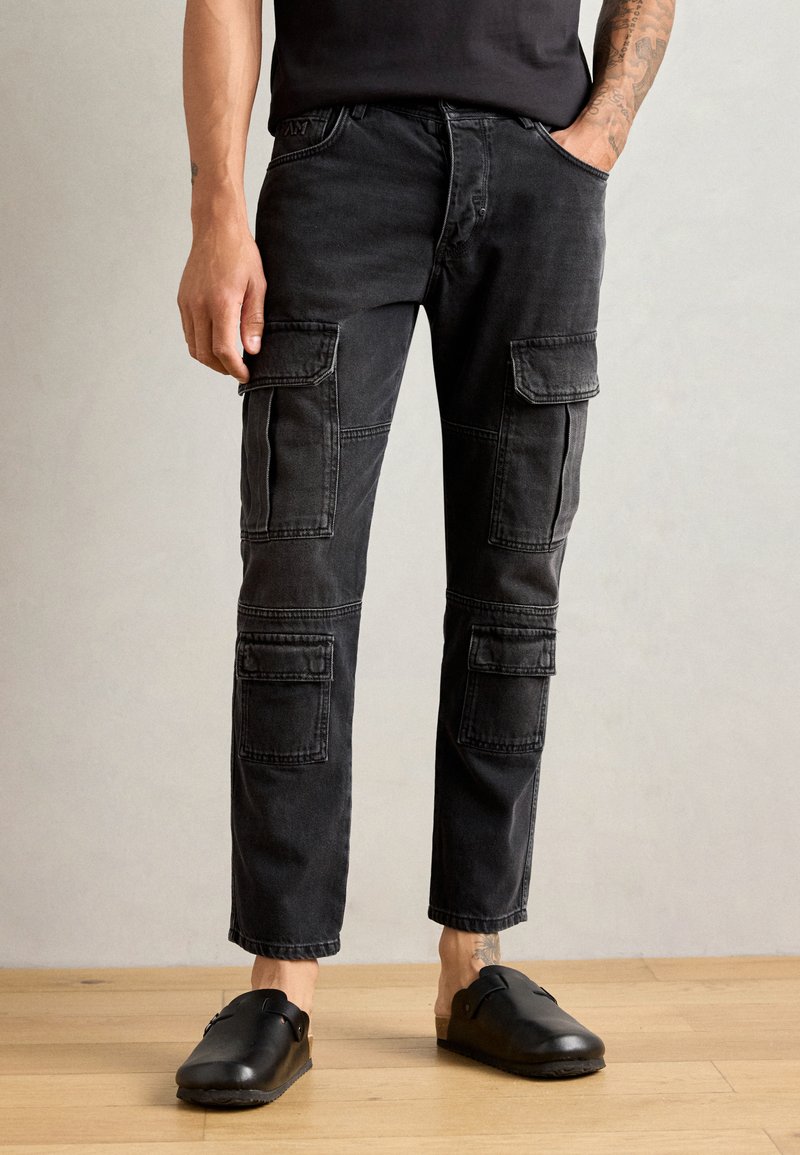 Pantaloni cargo neri in denim con molteplici tasche applicate, design a gamba dritta e leggere usure. Abbinati a zoccoli neri.