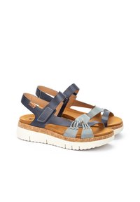 Sandalias de tiras en azul marino y celeste con entresuela de corcho, plantilla marrón y suela de goma blanca. Presentan un detalle trenzado en las correas.