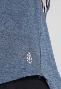 Blå heathered t-shirt med en silverlöv-logotyp på nederdelen, mjuk textur, korta ärmar och en avslappnad passform.