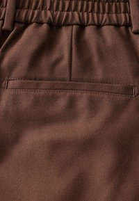 Tessuto marrone con una finitura liscia e testurizzata. Una tasca posteriore piatta è visibile, integrata senza soluzione di continuità nel materiale.