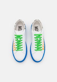 Białe trampki z zielonymi sznurówkami, niebieskimi podeszwami i pomarańczowym napisem. Napis pojawia się z boku. Wnętrze ma wzorzystą podszewkę.