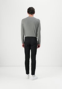 Grå långärmad skjorta som kombineras med svarta slim-fit byxor och vita sneakers. Skjortan har en rund hals och är gjord av ett mjukt material.