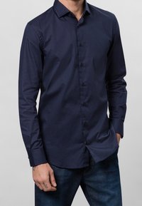 Marinblå långärmad skjorta av mjukt tyg, med knappslå framtill, kontrasterande svarta knappar och en klassisk krage.