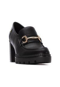 Mocassini neri in pelle con tacco, caratterizzati da una fibbia dorata, suola piatta rigata e tacco a blocco chunky. Texture liscia con dettagli di cucitura.
