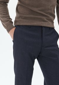 Námořnické modré strukturované kalhoty slim fit s zipovým zapínáním a diskrétními bočními kapsami, v kombinaci s hnědým upnutým svetr.