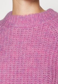 Pull en tricot rose avec une texture côtelée, un col rond et un matériau doux et duveteux présentant de légères variations de couleur.