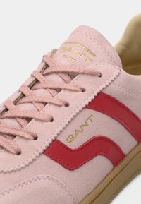 Sneakers in camoscio rosa con dettagli rossi, marchio dorato, lacci testurizzati e suola in gomma. Il motivo laterale è ondulato.