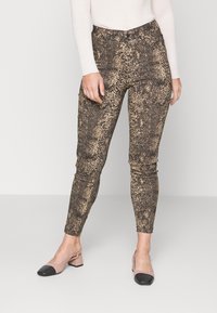 Taperade byxor i ett svart och beige ormskinnsmönster, med en mjuk textur och hög midja, kombinerade med tvåfärgade klackskor.