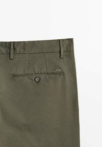 Pantaloni in cotone verde oliva con una texture liscia, dotati di una tasca posteriore con chiusura a bottone e un piccolo etichetta del marchio sul lato.