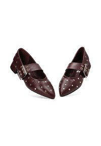 Zapatos Mary Jane de punta en rojo oscuro con tachuelas plateadas y grandes hebillas laterales sobre tacones bajos de bloque.